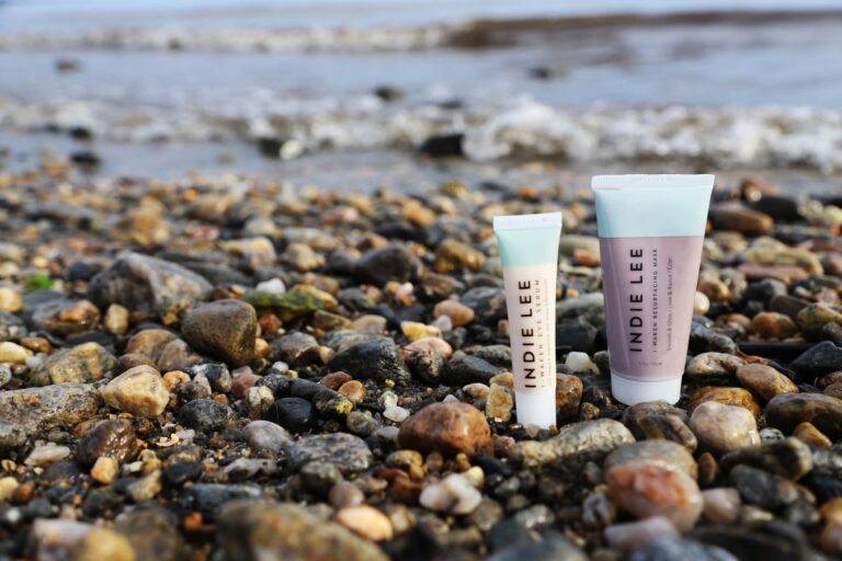 Indie Lee products on rocks on the beach.