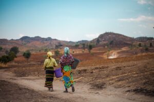 Two women carrying buckets on a dry landscape in Malawi.