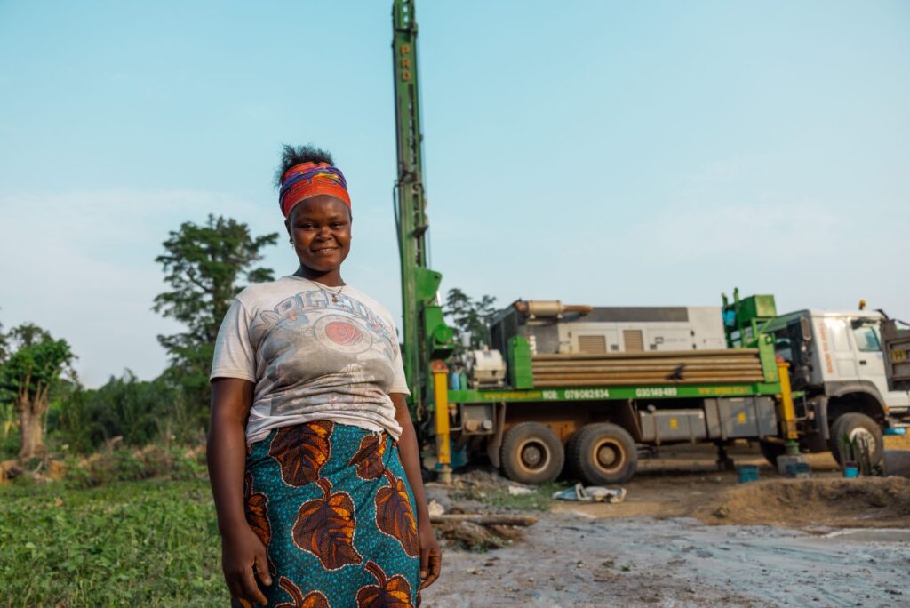 A woman smiling in front of a truck drilling a well in Sierra Leone.